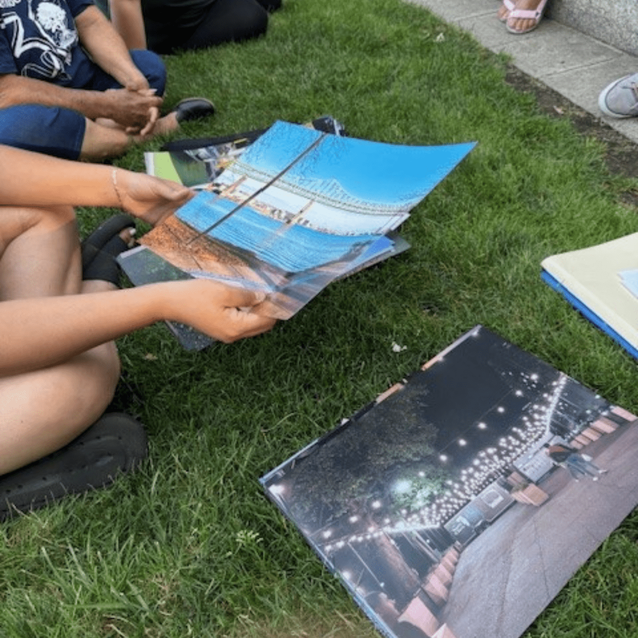 A group of people sitting on the grass, sharing and looking at pictures together in a relaxed outdoor setting.