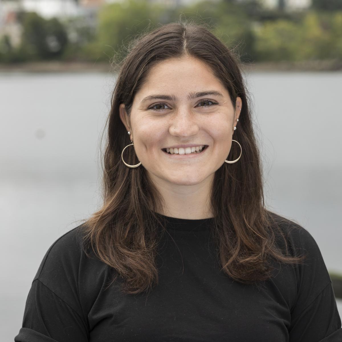 A photo of a person with their hair parted in the middle and a black top standing in front of the Chelsea Creek.