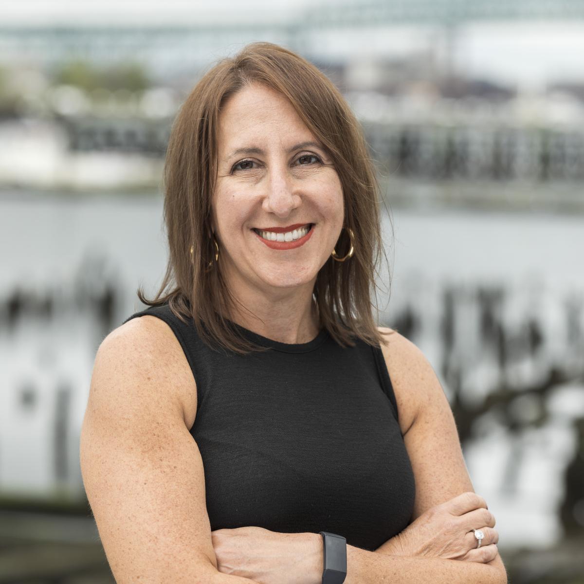 A woman wearing a black tank top and has her arms crossed in front of the Chelsea Creek.