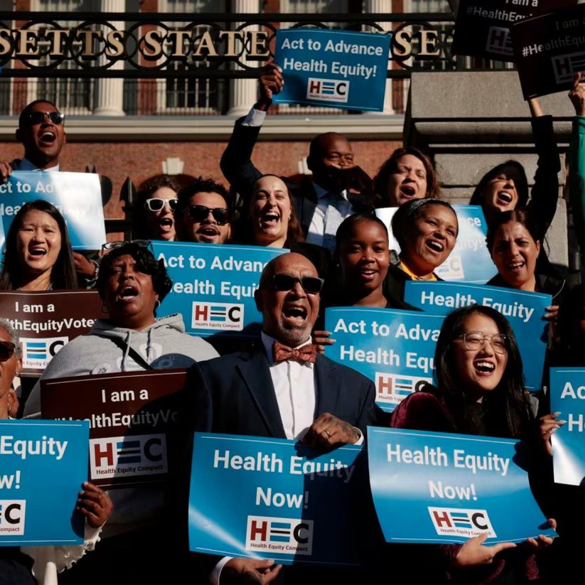 Diverse group of activists holding signs that read "Health Equity Now!" in front of the Massachusetts State House.