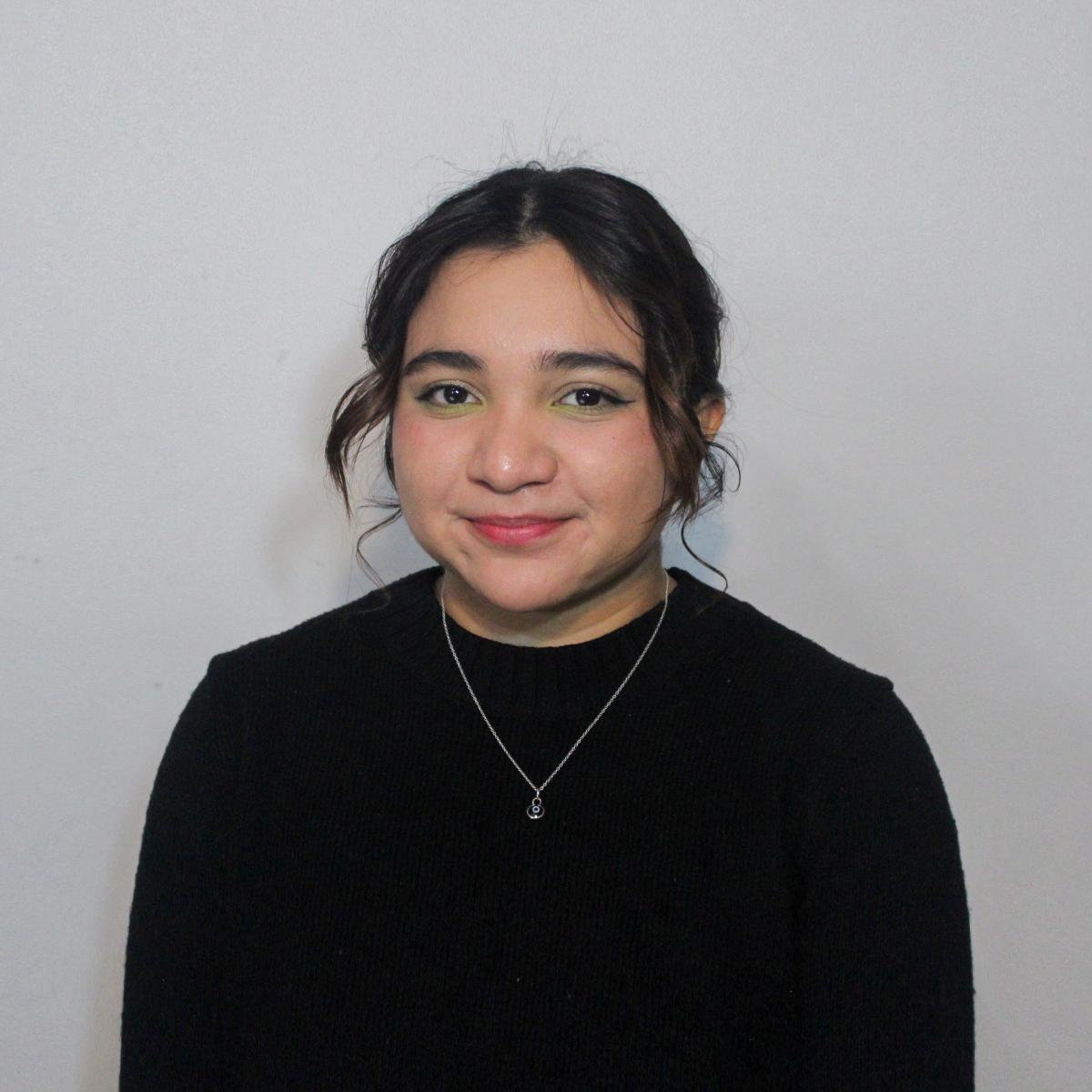Smiling young person wearing a black sweater against a white wall.