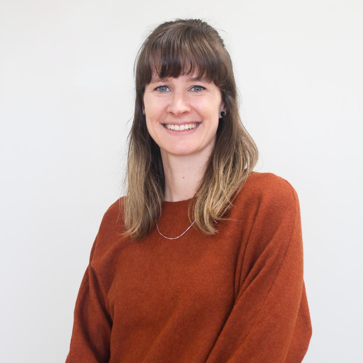 Smiling white woman wearing a dark orange sweater against a white background.