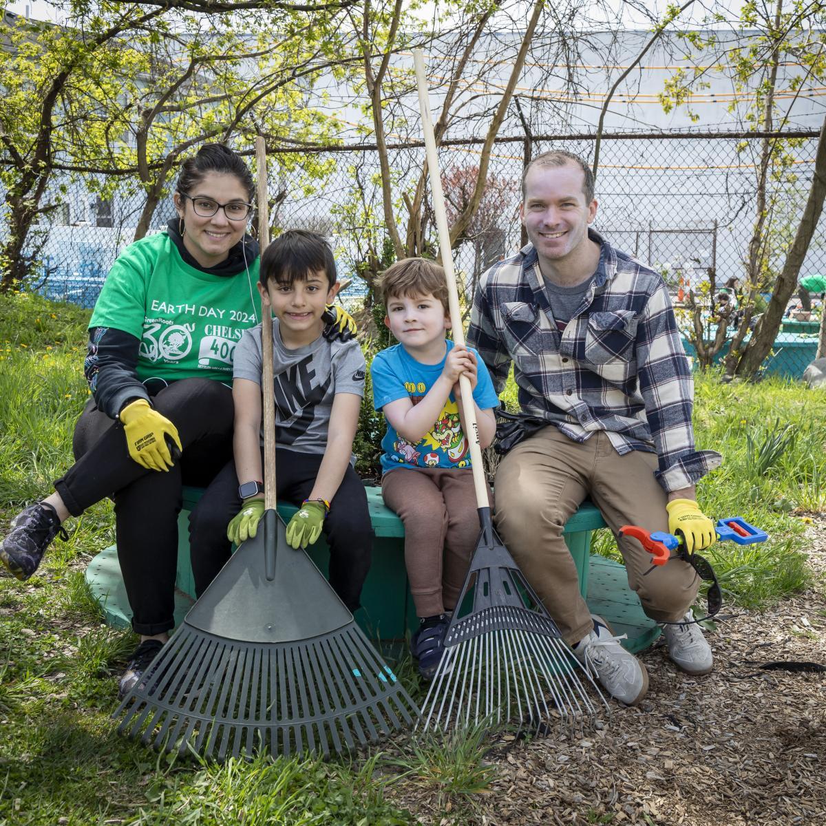 A family of four holding rakes at a cleaning event in a park.