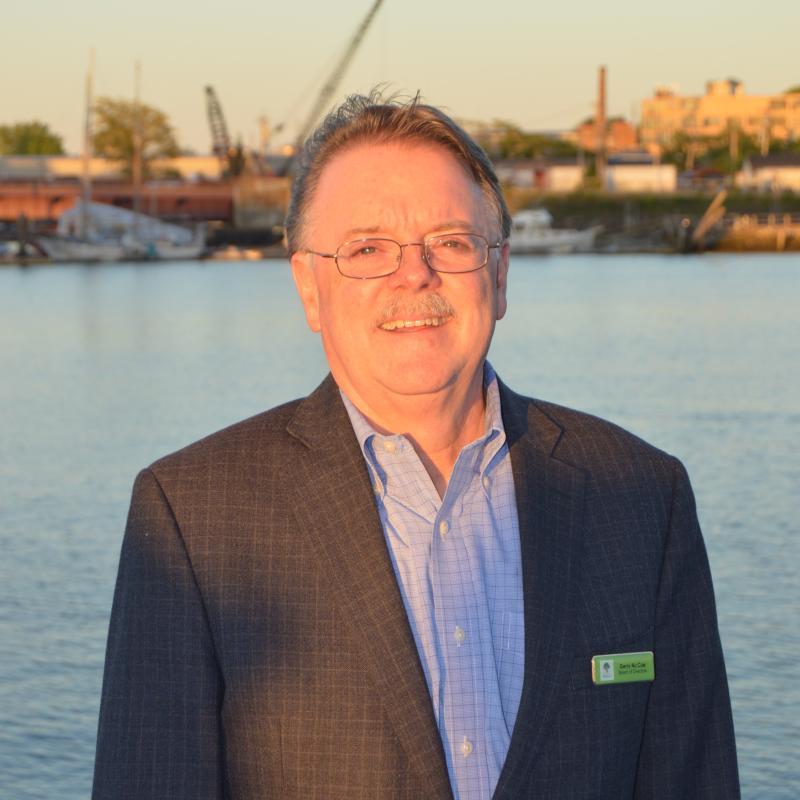 A man with a blue top and black blazer standing in front of the water.