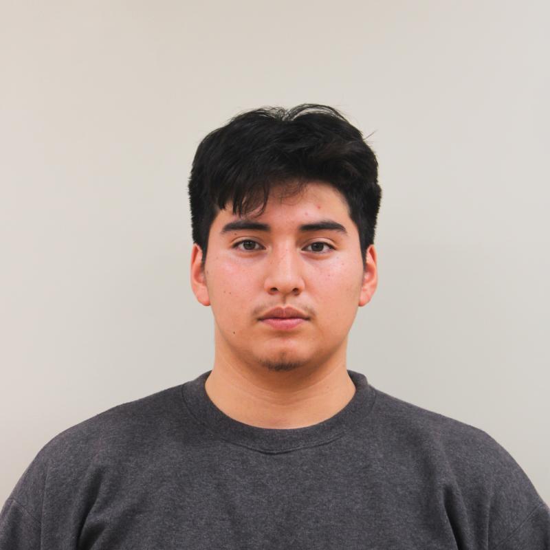Teenage boy wearing a dark gray sweater standing against a white wall.
